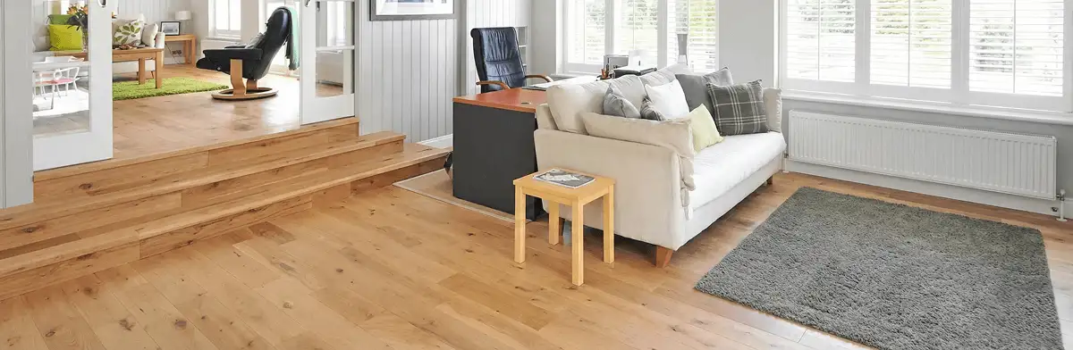 A modern living room with professionally installed laminate flooring, a beige sofa, a small side table, a gray rug, and large windows with white shutters in Saint Petersburg, FL